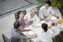 Familia multi-generación china sentada en la mesa de comedor en el patio - foto de stock