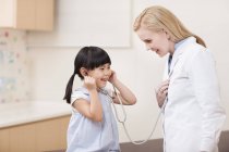 Female doctor playing with girl with stethoscope — Stock Photo