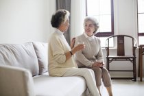 Senior mujeres chinas hablando con té en el sofá - foto de stock