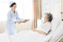 Chinese nurse serving food for senior patient — Stock Photo