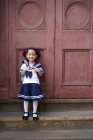 Chinese elementary age girl in school uniform leaning on door — Stock Photo