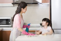 Contador de cocina de limpieza de madre e hija china con botella de aerosol - foto de stock