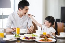 Chinese daughter feeding father with chopsticks at lunch — Stock Photo