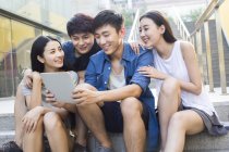 Chinese friends using digital tablet and looking down — Stock Photo