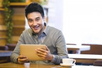 Chinese man listening to music with digital tablet in coffee shop — Stock Photo