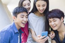 Chinesische Freunde schauen aufs Smartphone und lächeln — Stockfoto