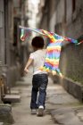 Мальчик бежит с цветным воздушным змеем в переулке, вид сзади — стоковое фото