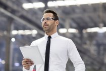 Бізнесмен в захисних окулярах тримає цифровий планшет на заводі — стокове фото