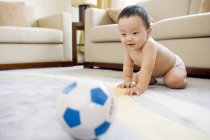 Bebé chino jugando con pelota de fútbol en la sala de estar - foto de stock