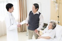 Chinese doctor talking with senior couple in hospital — Stock Photo