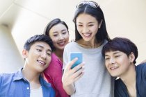 Китайские друзья смотрят на смартфон и улыбаются — стоковое фото