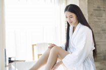 Chinesische Frau sitzt auf Badewanne und schaut nach unten — Stockfoto