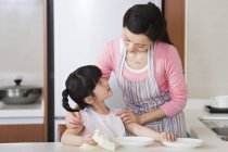 Chinese girl drying plates with mother — Stock Photo