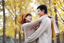 Casal chinês com sacos de compras abraçando no parque — Fotografia de Stock