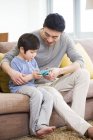 Китайский отец и сын играют в видеоигры на диване — стоковое фото