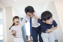 Padre chino abrazando hermanos en casa y riendo - foto de stock