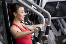 Mulher chinesa usando máquina de exercício, vista lateral — Fotografia de Stock