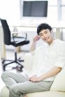 Young Chinese man sitting on sofa in living room — Stock Photo