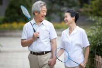 Senior Chinese couple walking in residential district with badminton rackets — Stock Photo