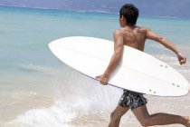 Joven chino corriendo con tabla de surf en el agua - foto de stock