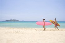 Pareja china con tablas de surf caminando en la playa en China - foto de stock