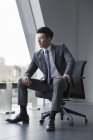 Chinesischer Geschäftsmann blickt durch Fenster im Büro — Stockfoto