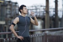 Chinese man resting after exercising on street and drinking water — Stock Photo
