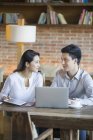 Chinese man and woman sitting in cafe with laptop — Stock Photo