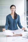 Chinese woman meditating on office table — Stock Photo