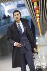 Uomo d'affari cinese che cammina in aeroporto con valigia e passaporto — Foto stock