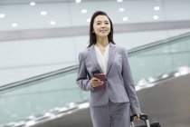Chinese businesswoman walking in airport with suitcase and passport — Stock Photo