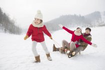Chica china tirando del trineo con los padres en la nieve - foto de stock