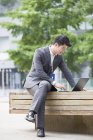 Empresário chinês trabalhando com laptop no banco de rua — Fotografia de Stock