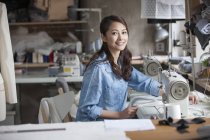 Diseñador de moda chino trabajando con máquina de coser en estudio - foto de stock