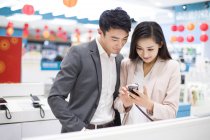 Pareja china mirando teléfono inteligente en la tienda de electrónica - foto de stock