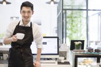 Chinese coffee shop owner at counter with cup of coffee — Stock Photo