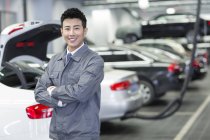 Chinese auto mechanic standing in workshop with arms folded — Stock Photo