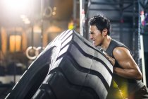 Chinese man pushing large tire in crossfit gym — Stock Photo