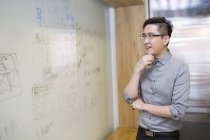 Chinese man thinking in front of whiteboard — Stock Photo