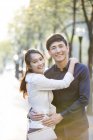 Китайська пара обіймаються на вулиці і, дивлячись в камери — стокове фото