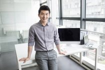 Empresário chinês apoiado na mesa no escritório — Fotografia de Stock