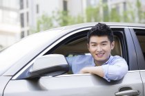 Hombre chino sentado en coche y mirando en la cámara - foto de stock