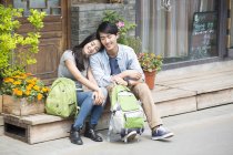 Chinese couple resting on street with backpacks — Stock Photo