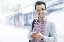 Hombre chino sosteniendo teléfono inteligente y sonriendo - foto de stock