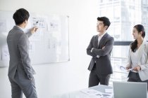 Chinese business people talking at whiteboard in meeting room — Stock Photo