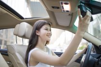 Chinese woman adjusting mirror in car — Stock Photo
