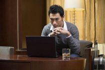 Empresário chinês usando laptop à mesa no quarto de hotel — Fotografia de Stock