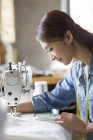 Chinese female tailor using sewing machine, side view — Stock Photo