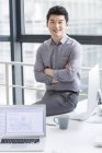 Chinese businessman sitting on office table with arms folded — Stock Photo