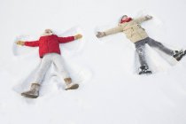 Niños felices haciendo ángeles de nieve - foto de stock